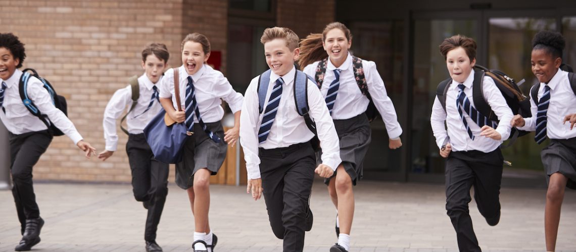 Group Of High School Students Wearing Uniform Running Out Of School Buildings Towards Camera At The End Of Class